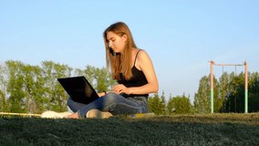 a young woman works on a computer in a park, drinks juice