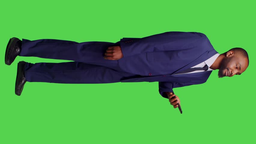 Vertical video: Side view of company employee talking on smartphone call in studio, having remote conversation on telephone line. Office worker using mobile phone over full body green screen backdrop