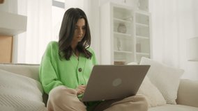 Excited young woman looks at laptop celebrates online success win. Euphoric lady gets new distance job opportunity sits on sofa at home. Motivated girl reads good news in email, happy about victory 4K