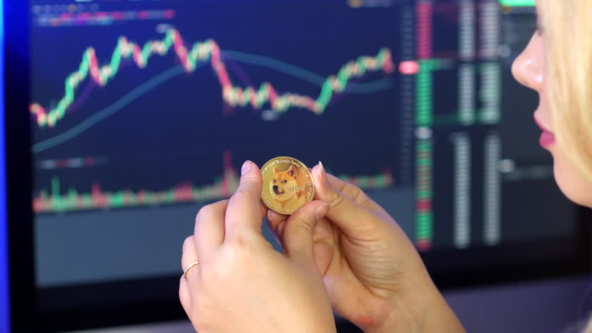 Blonde woman holding and looking at dogecoin in her hands in front of cryptocurrency trading graphs. | Shutterstock HD Video #1102104685