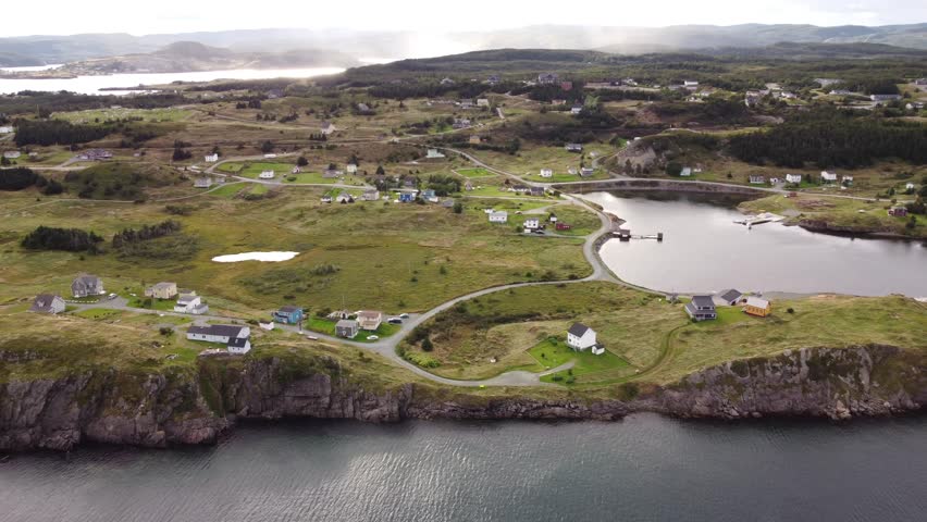 Aerial small colourful homes dotted across rolling hills overlooking high rocky cliffs near Trinity Newfoundland Canada.
