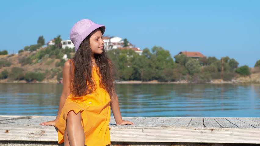 Sit on piers against bay. A pensive calm child sit on piers against green tropical bay under sun.