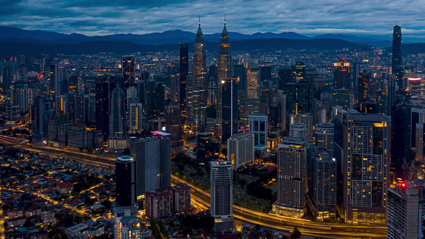 Aerial Drone Time lapse: High angle drone view during a cloudy dawn overlooking Kuala Lumpur city skyline against mountains background in Malaysia. Zoom out motion timelapse. Prores 4KUHD
