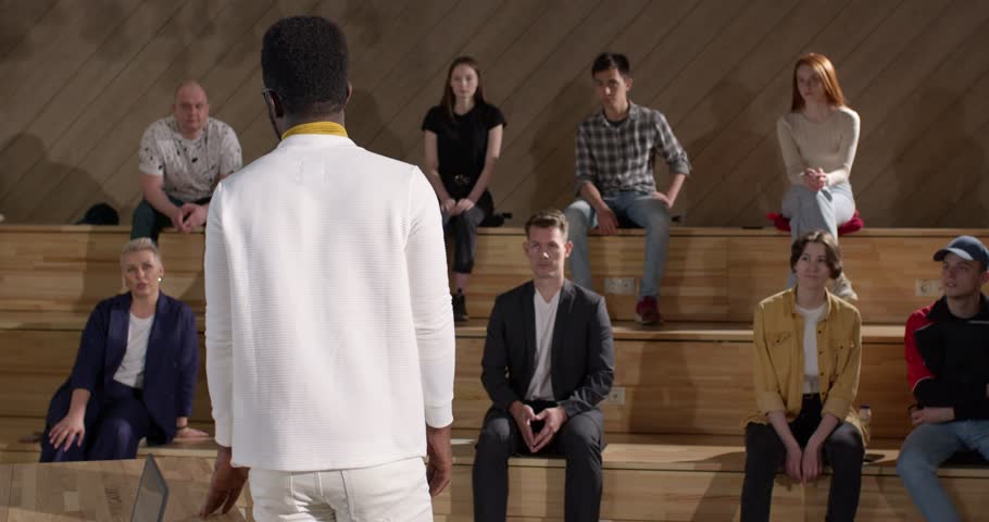 Rear View Lecturer Man Of African Appearance Give Speech To Students, Group Of People. Handsome Black Male In White Suit At Business Event, Give Necessary Information To Future Enterpreneurs, Talking