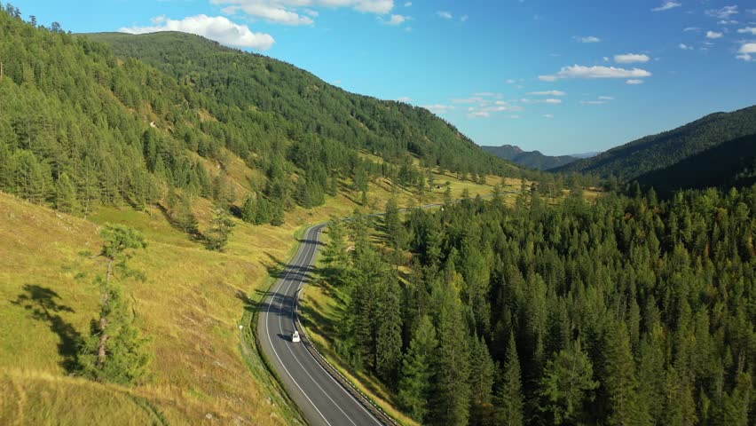 White SUV van riding on asphalt road surrounded picturesque fir forest autumn mountain scenery with river travel journey aerial view. Drone cinematic minivan car alpine landscape exploration vacation