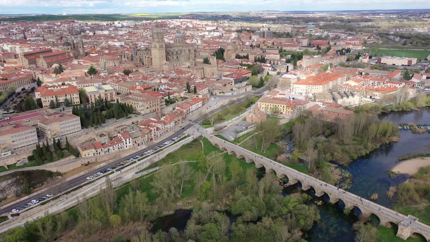 Scenic aerial view of Salamanca historic district overlooking gothic building of cathedral towering over residential buildings and ancient arched roman bridge across Tormes river in spring, Spain