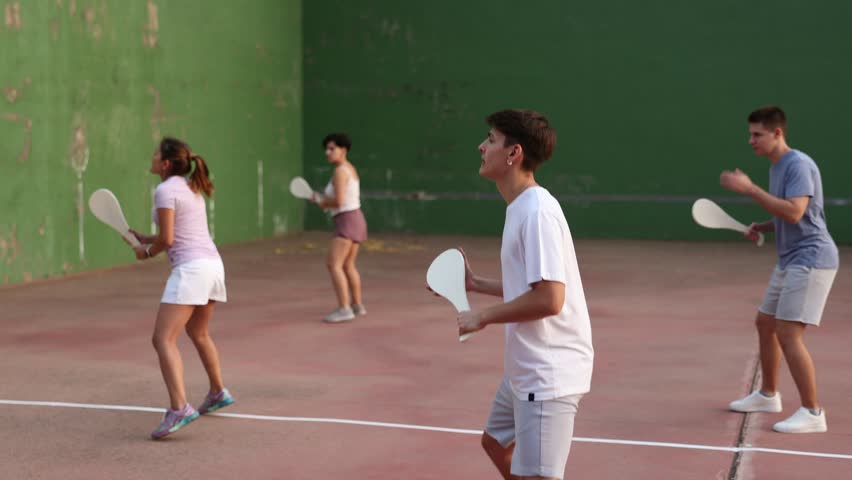 Group of sporty young people serving ball with special equipment, wooden paleta, during Basque pelota game outdoors. Boy playing pelota on outdoor fronton. Royalty-Free Stock Footage #1102113611