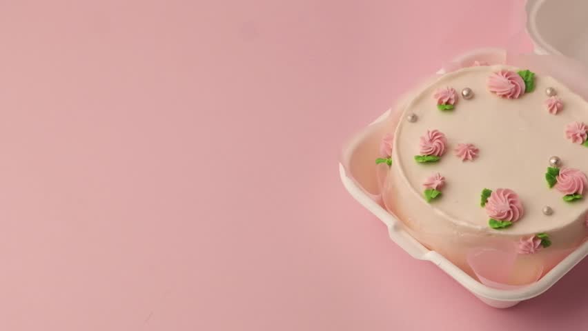 Small traditional Korean style bento cake with white cream cheese frosting decorated with pink whipped cream flowers. Little spring cake in the white gift box on the pink pastel background. Top view