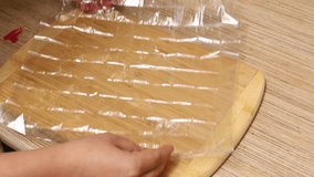 Video tutorial of unrecognizable female hands holding transparent plastic baking bag, showing red clips as lock on wooden table in domestic kitchen. Master class, step by step, culinary school. 4k