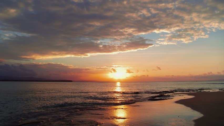 Landscape view of calm waves of sea water with orange sunlight at sunset. Evening beach on the island. exotic coast. Summer holidays, rest in amazing picturesque nature. Relaxing paradise. Twilight.