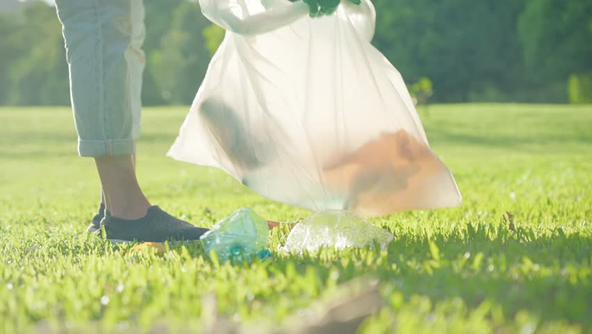 Closeup shot of female volunteer gloved hands woman walking collecting in bag a trashes on green grass area inside the public park during the sunny day. Plastic pollution. Environmental problem.  Royalty-Free Stock Footage #1102122509