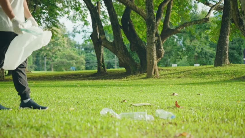 Full Length Asian young volunteer walking collecting in bag a trashes on green grass area inside the public park during the sunny day. Plastic pollution and environmental problem. Save the planet. Royalty-Free Stock Footage #1102122513