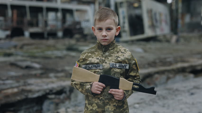 Portrait of the little usa soldier holding toy gun standing in ruins. Patriot. Warrior