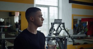 A fit young man staying hydrated while working out in a gym, promoting good health and strength. This video is ideal for promoting fitness and health-related products or services.