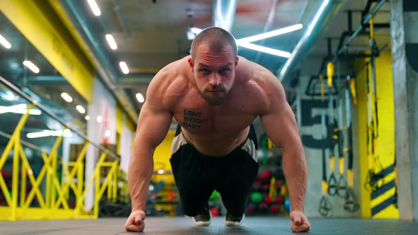 Bald bodybuilder exercising in the gym. Raises the barbell, dumbbells, jumping rope, trx workout. Pumped up big muscles. Work with large, heavy weights in the gym. Nice curvy body.