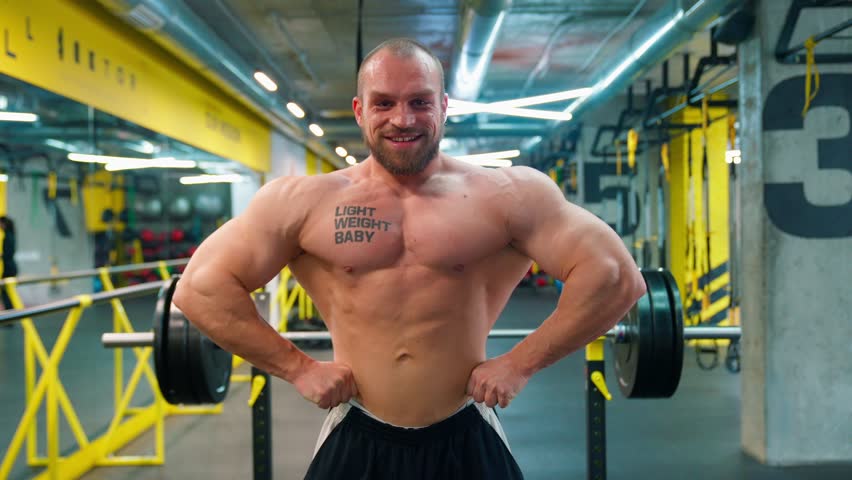 Bald bodybuilder exercising in the gym. Raises the barbell, dumbbells, jumping rope, trx workout. Pumped up big muscles. Work with large, heavy weights in the gym. Nice curvy body.