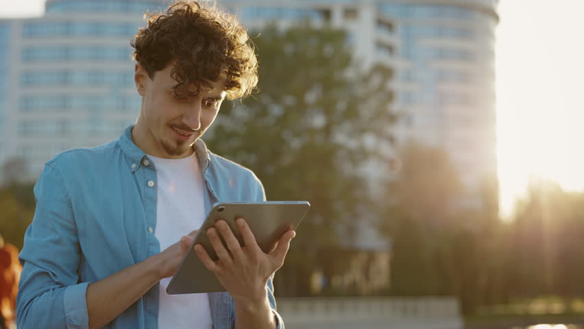 Caucasian Bearded Man Standing on the Street Surfing Internet on Tablet Computer Outdoors. Young Male Outside Using his Tablet, Texting With Friends. Male User Chatting Browsing Online Royalty-Free Stock Footage #1102134679