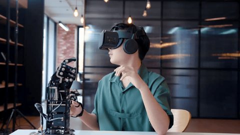 4K, Asian boy wearing a 3D ride around his eyes on head and have headphones attached player listen sound, wore a robot hand controller It is a hand robot intended for assisting disabled. Video stock