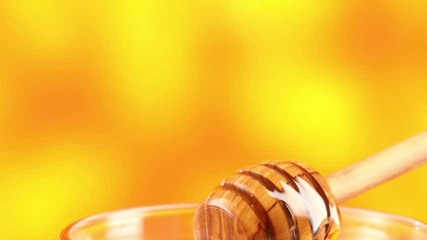 Honey dripping from honey dipper in glass bowl. Close-up. Healthy organic Thick honey dipping from the wooden honey spoon, closeup. jar on the wood table. organic food on color background.