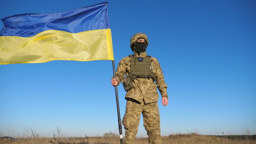 Ukrainian army man in military uniform lifting national banner. Young male soldier holds a waving flag of Ukraine against blue sky. Victory against russian aggression. Invasion resistance. Low view Royalty-Free Stock Footage #1102137525