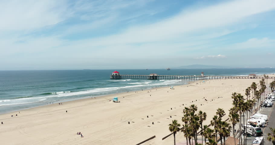 Shooting from below of Huntington Beach Pier with people and shopping areas. Aerial flyover and surveying of the pier and people on the Southern California coast, revealing a view of the Pacific Ocean