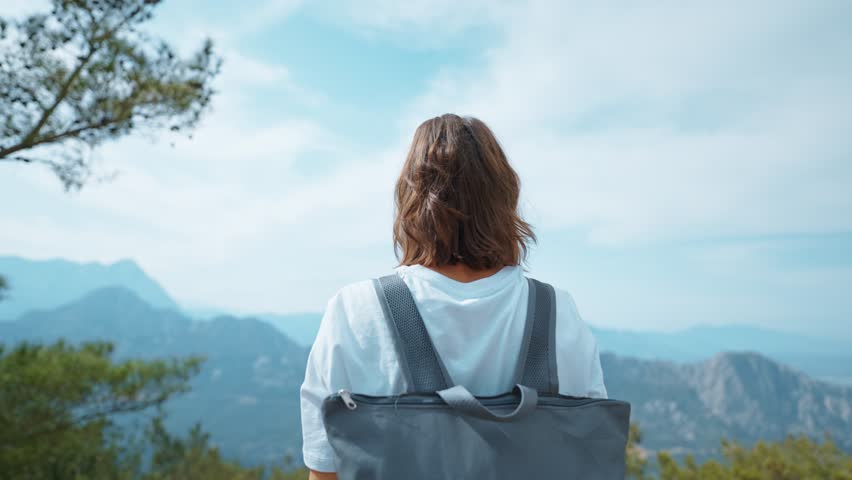 Female Tourist traveler on viewing platform on mountain top against blue background valley landscape view mockup for text. Fashion young girl in casual clothes enjoying a view from the mountain