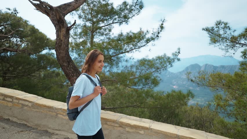 Female Tourist traveler on viewing platform on mountain top against blue background valley landscape view mockup for text. Fashion young girl in casual clothes enjoying a view from the mountain