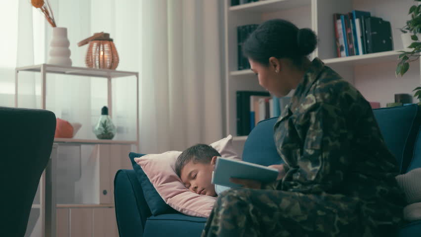 Loving mother in military uniform finishes reading book to son before sleep Royalty-Free Stock Footage #1102140577