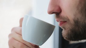 A man drinks coffee by the window in the morning. Close-up of a white cup and lips of a man drinking coffee - Powered by Shutterstock - Get 15% off with code: PIKWIZARD15