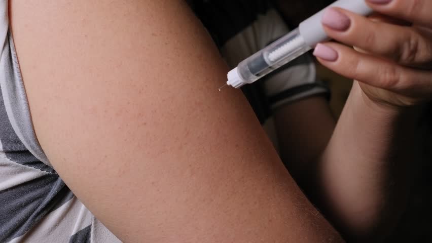Close-up of a young woman injecting insulin into her arm with an insulin pen at home. Treatment of diabetes. 