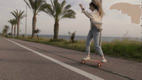 Hipster skateboarder woman skateboarding on city road with palm trees by the sea in spring