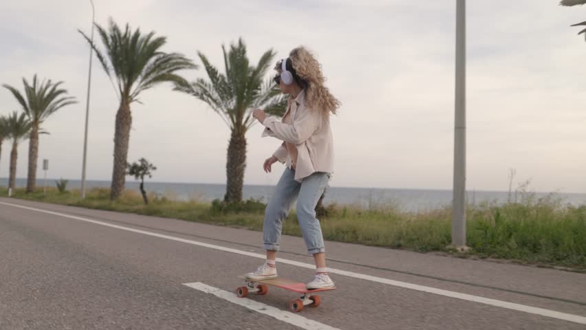 Young woman skater skateboarding and listening to music cruising down road, ecofriendly transportation concept