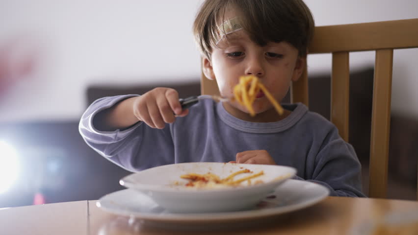 Male kid eating pasta spaghetti by himself. Child spinning pasta with hands and fork. One small boy eats Italian food for dinner Royalty-Free Stock Footage #1102146089