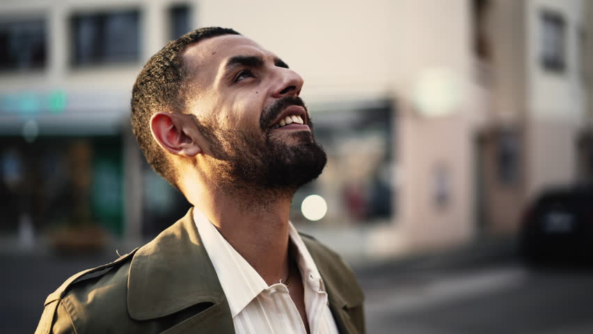 a young Arab man standing in the street, lost in thought as he gazes up at the sky. His expression is one of hope and contemplation, suggesting that he is pondering his future with a positive outlook Royalty-Free Stock Footage #1102146129