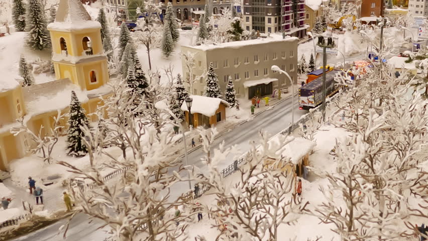 Snowy town in winter with buildings, roads, snowing trees and moving cars, trucks. Street of city center in usual everyday life. Winter season in a city with snow-covered houses and roads.