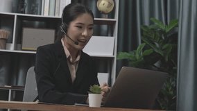Businesswoman wearing headset and microphone working at her desk and using laptop. Enthusiastic female employee utilizing laptop for remote online meeting, business video conference in the office.
