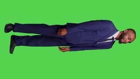 Vertical video: Side view of optimistic startup manager sending air kisses in studio, standing over full body greenscreen, doing romantic gesture. Male employee in office suit with kissy face being