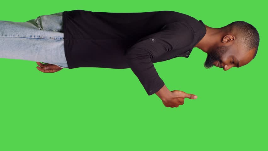 Vertical video: Profile of casual person giving thumbs up on camera, showing successful gesture and agreement. Young man doing like okay symbol with approval, standing over green screen background