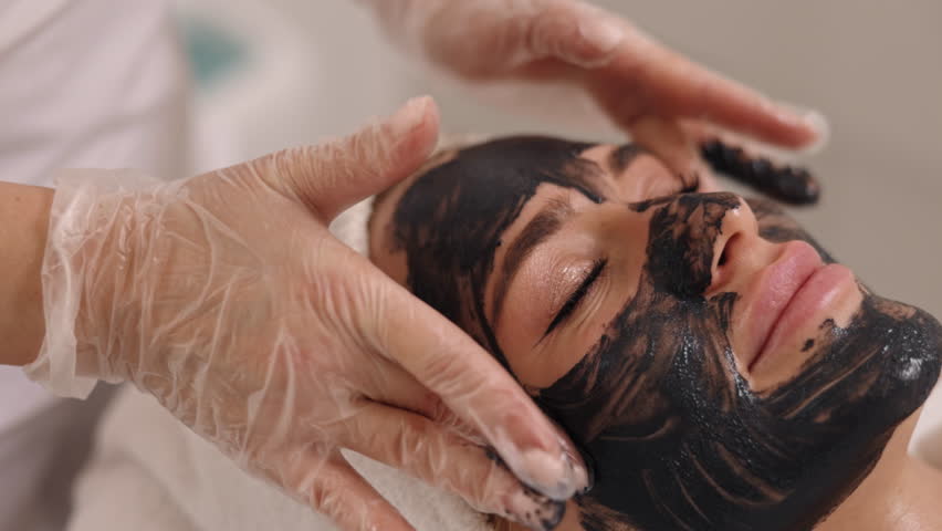 Black mask, Kelp rejuvenation, Cleansing treatment. Beauty salon, skincare expert applies black mask to client's face, offering facial detox, lifting, kelp rejuvenation, mud therapy | Shutterstock HD Video #1102148881