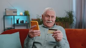 Grandfather senior man using credit bank card and smartphone while transferring money, purchases online shopping cashless, order food delivery, pay bills at home apartment indoor. Elderly guy on couch - Powered by Shutterstock - Get 15% off with code: PIKWIZARD15