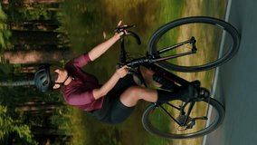 Woman riding road bicycle in forest. Vertical video. Cyclist twists pedals on bike along empty asphalt road. Cycling adventures. Recreation activity. Sport training. Fitness exercises