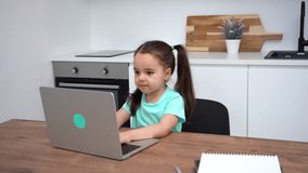 Cute little girl using a laptop, studying online at home, typing on keyboard.