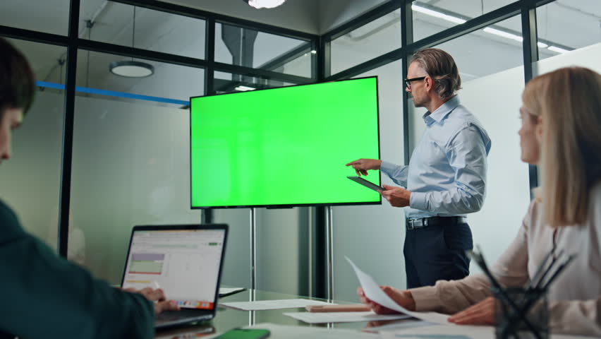 Businessman making chromakey presentation at modern office. Eyeglasses specialist pointing hand at green screen tv holding tablet. Business coach telling information to colleagues. People listening Royalty-Free Stock Footage #1102151051