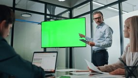 Businessman making chromakey presentation at modern office. Eyeglasses specialist pointing hand at green screen tv holding tablet. Business coach telling information to colleagues. People listening - Powered by Shutterstock - Get 15% off with code: PIKWIZARD15