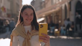 Happy woman with hearing disorder saying phrase Thanks for help with sign language while having video call outdoors. Young female walking on city street and using smartphone for conversation.