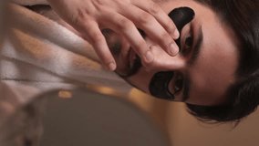 Vertical video. Eye patches. Facial care. Anti-aging skincare. Confident man with stubble mustache applying moisturizing black hydrogel pads touching face skin. - Powered by Shutterstock - Get 15% off with code: PIKWIZARD15