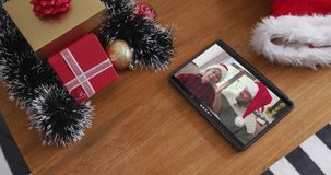 Smiling caucasian father and son wearing santa hats on christmas video call on tablet. christmas, festivity and communication technology.