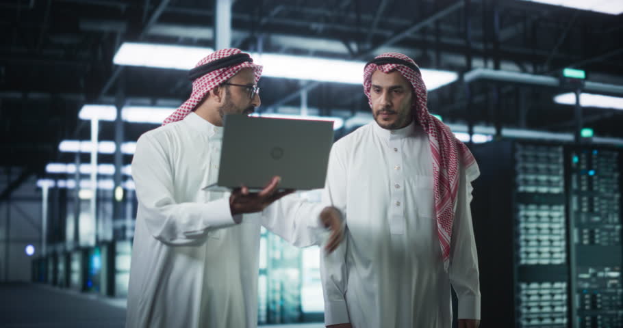 Middle Eastern Computer Engineer and Cybersecurity Specialist Work in Server Room, Talk, Perform System Maintenance Check with Laptop Computer. Specialists Doing Database Diagnostics in Data Center Royalty-Free Stock Footage #1102169025