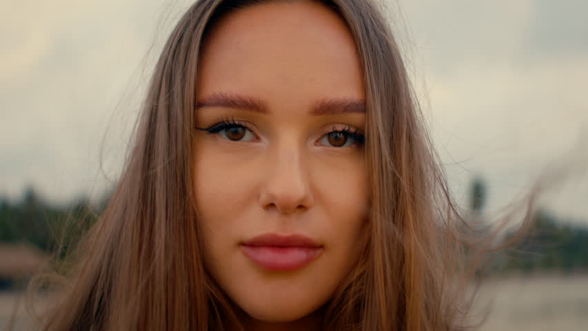 a beautiful girl with long straight hair stands on the beach and looks at camera