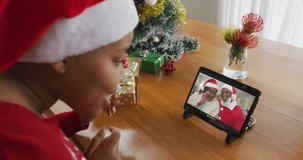 African american woman with santa hat using tablet for christmas video call with couple on screen. christmas, festivity and communication technology.